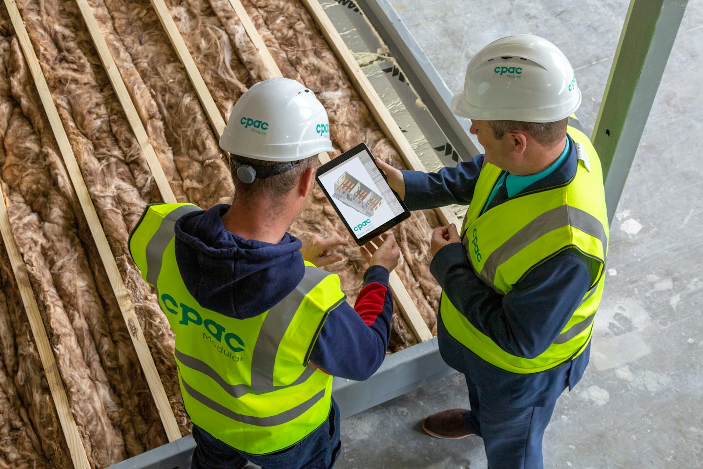Construction workers review building plans on a tablet.