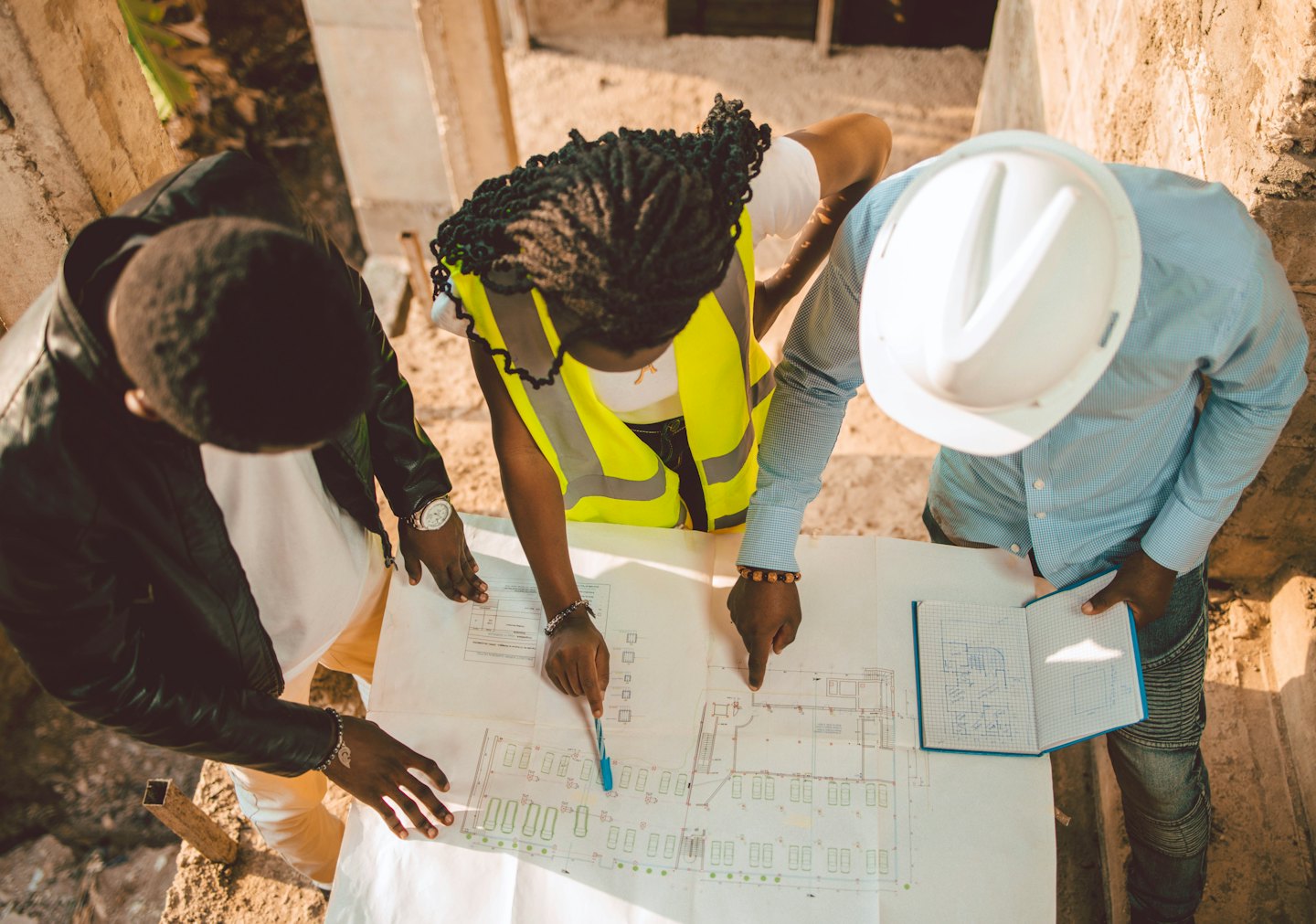 Quote Three construction professionals review blueprints on a concrete site.